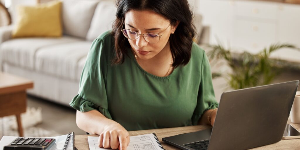 Woman studies financial document while using a laptop
