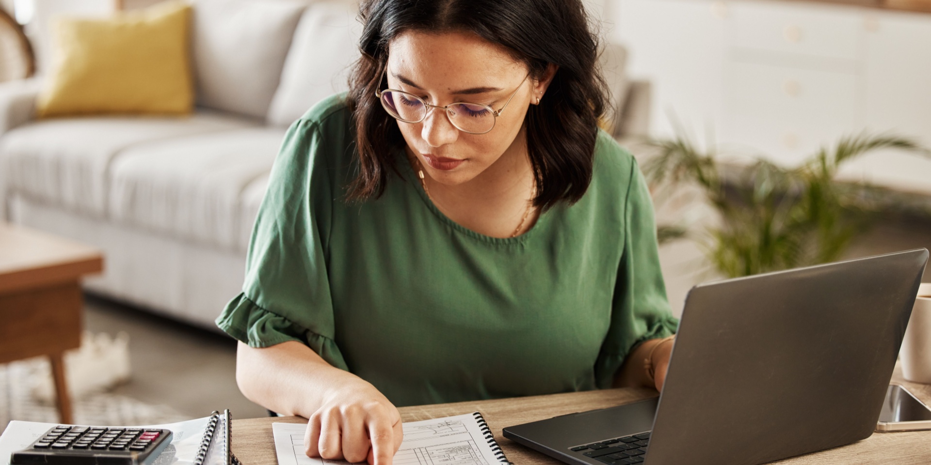 Woman studies financial document while using a laptop