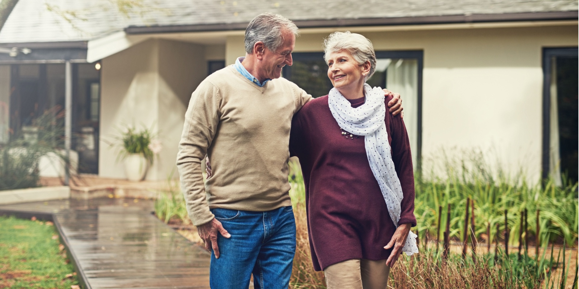 Senior couple walking outside their home, with their arms around each other